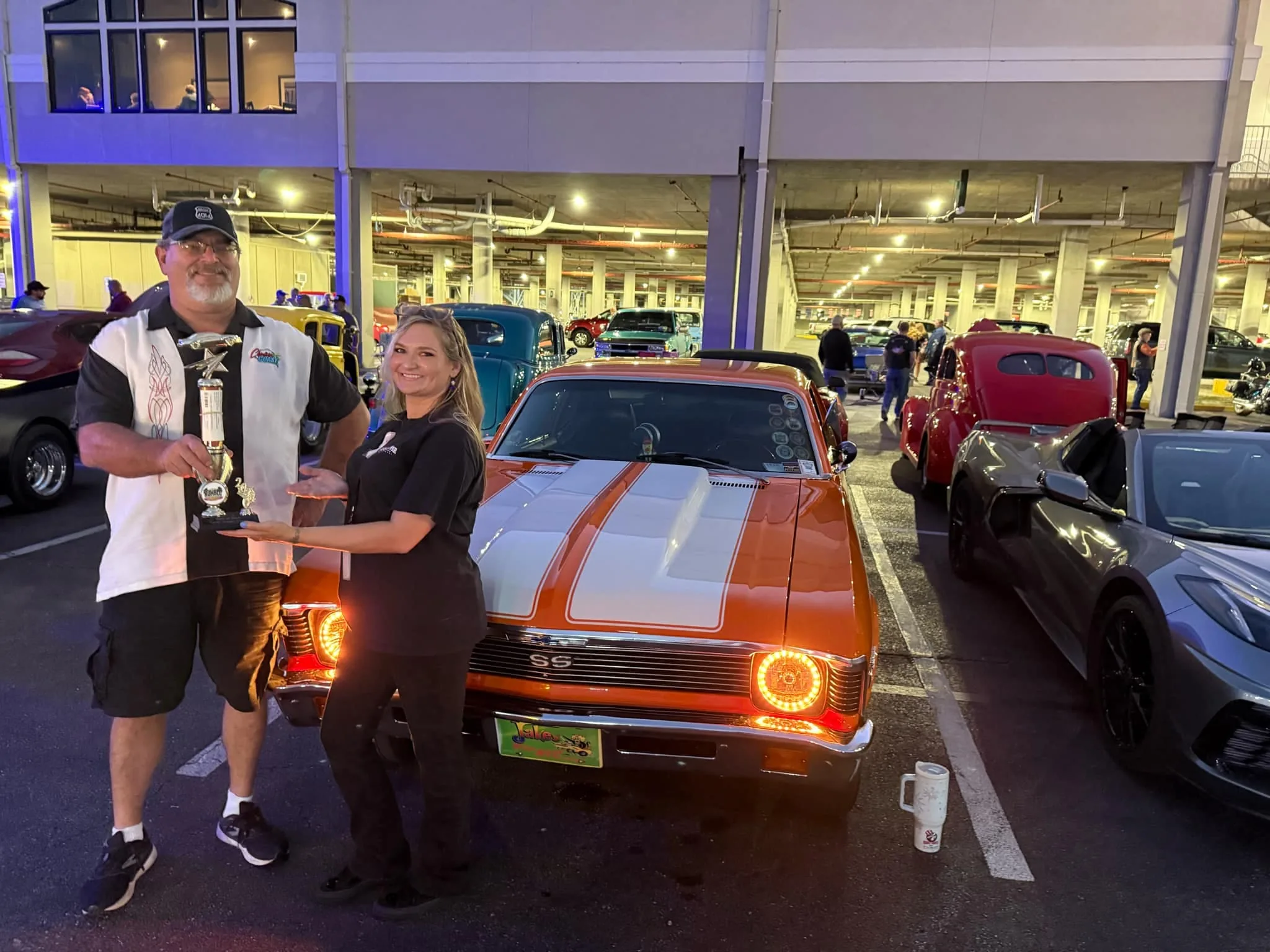 Prize winners holding an award beside an orange classic car