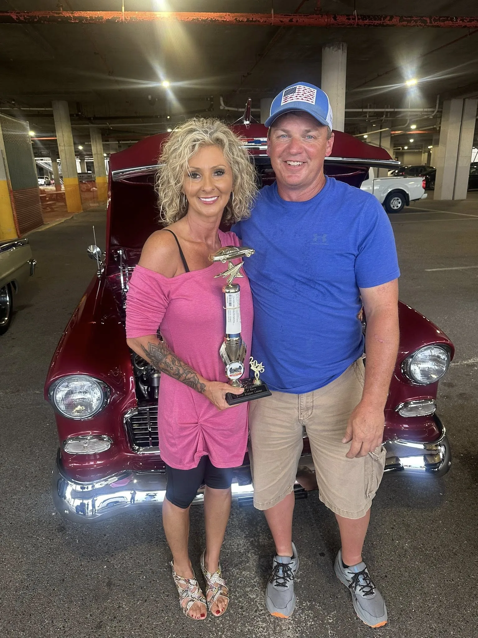 Prize winner holding a trophy beside a classic car